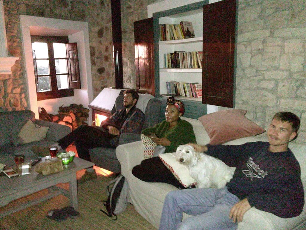 Casa Pardal coliving guests relaxing in the stone-walled living room, watching a movie together by the fireplace during a cozy evening in Catalonia.