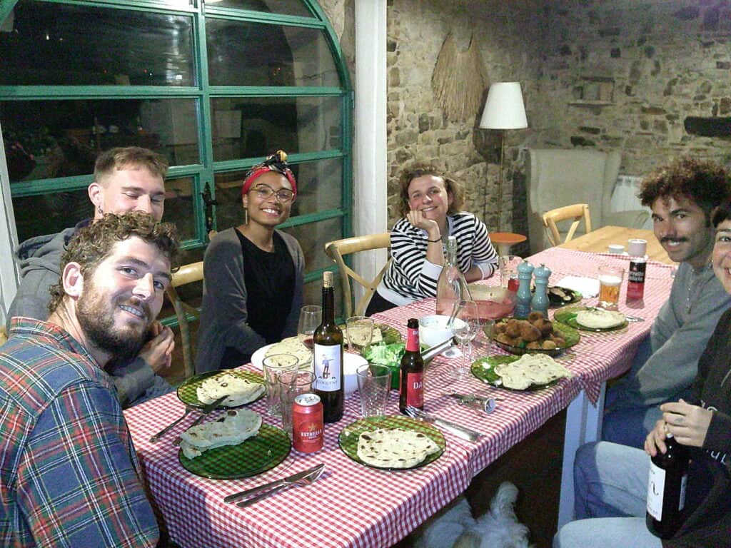 Casa Pardal coliving guests enjoying a shared dinner around a long table, gathered in a rustic stone dining room in Catalonia.