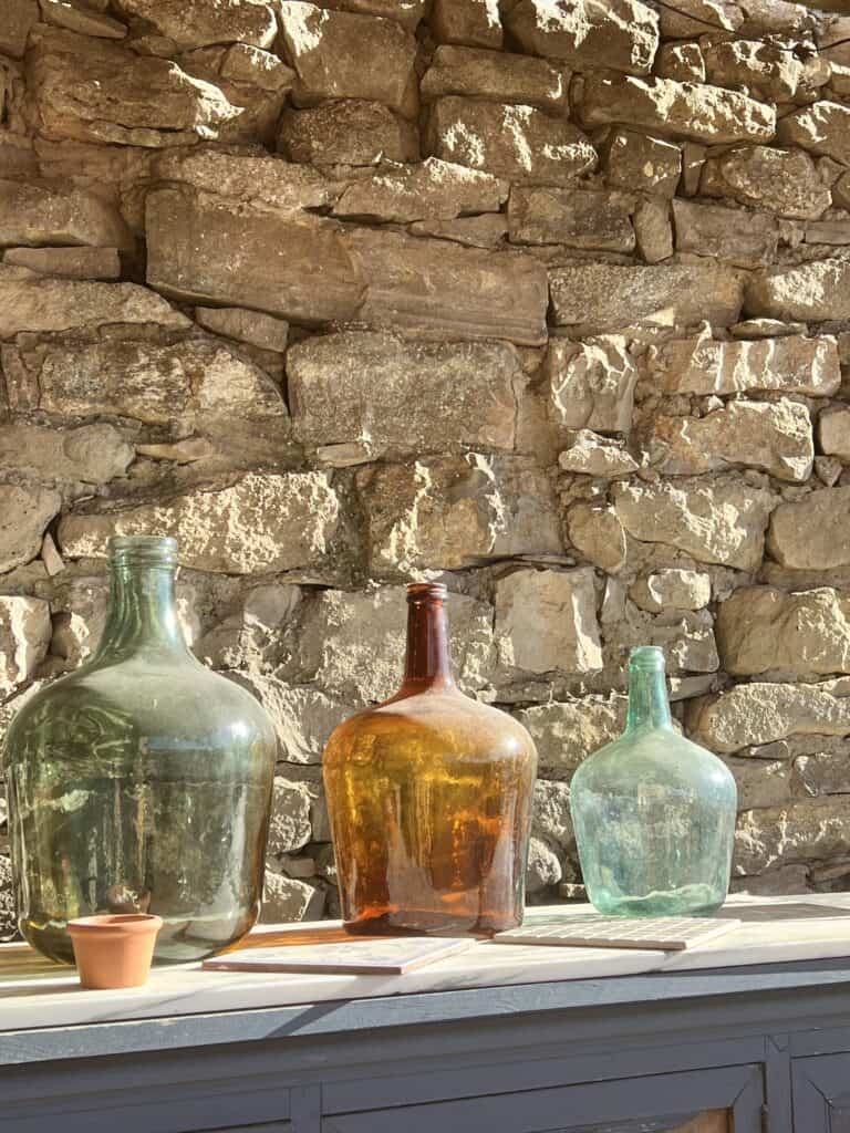 Morning sunlight reflecting through vintage glass bottles against a rustic stone wall at Casa Pardal.