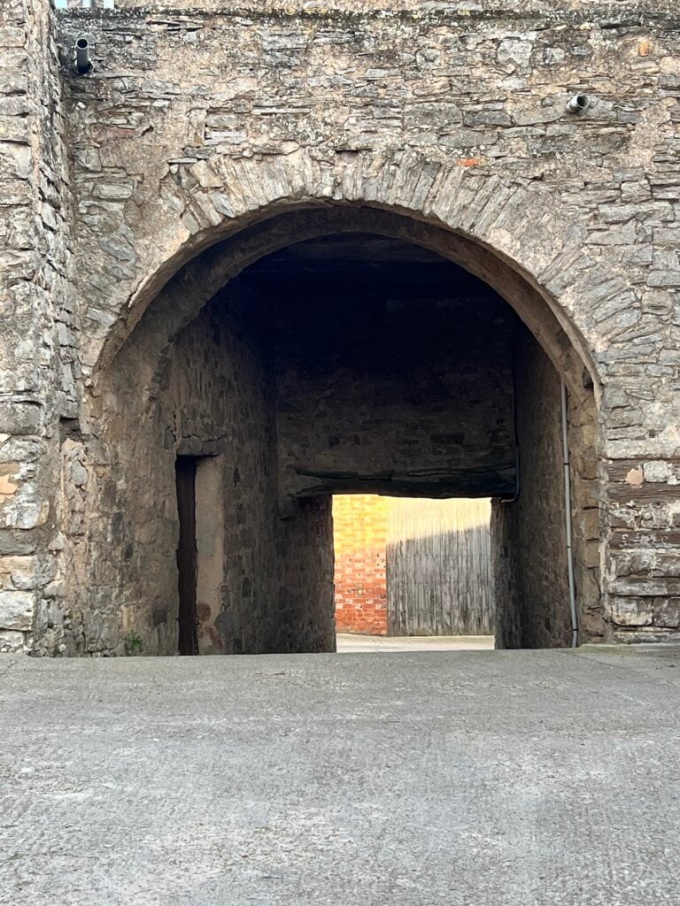 Stone archway entrance at Casa Pardal, a rural coliving house in Catalonia, Spain, with golden light visible through the passage.