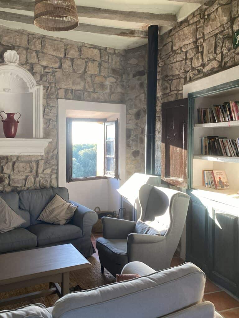 Cozy stone-wall living room at Casa Pardal with soft seating, a fireplace, and natural light coming through the doorway.