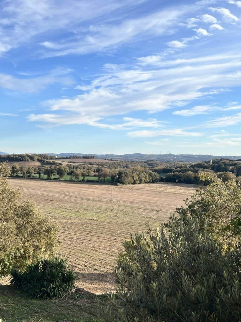 Wide countryside view of Catalonia's rolling fields and distant hills seen from Casa Pardal, with blue skies and soft clouds above.