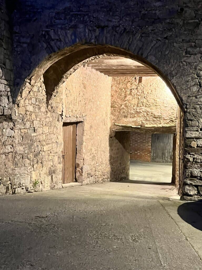 Evening view of Casa Pardal's old stone archway, lit by warm lights that reveal the texture of the rustic walls and historic architecture. 