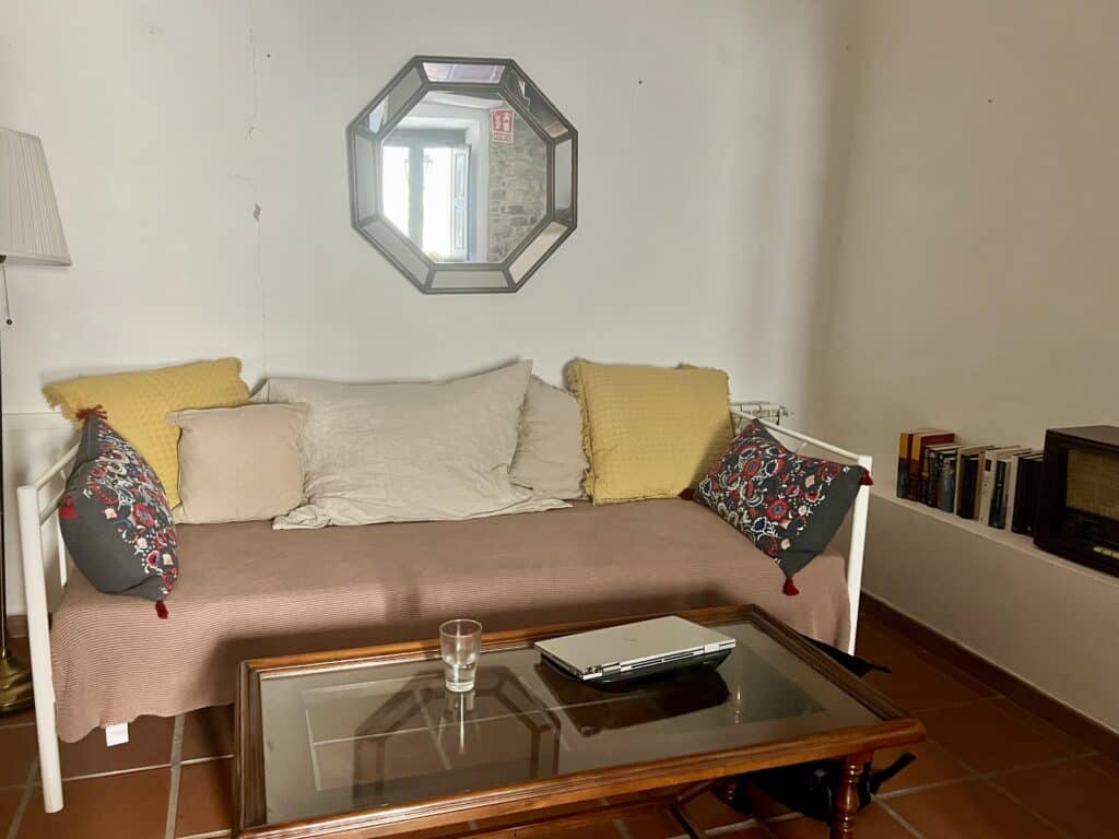 Cozy workspace inside Casa Pardal with a cushioned daybed, soft-toned pillows, a wooden coffee table, and natural light reflecting through an octagonal mirror.