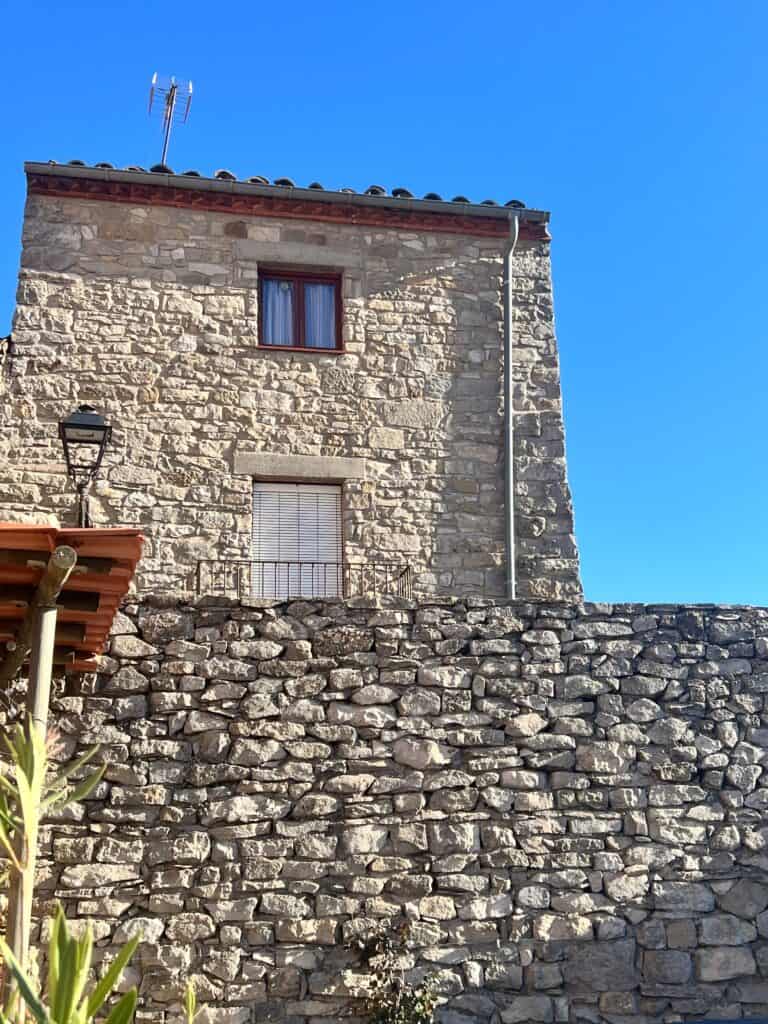 Stone facade of Casa Pardal against a bright blue sky, showcasing the rustic architecture and warm arrival atmosphere of the coliving house in Catalonia.