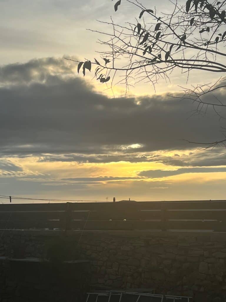 Sunset view from Casa Pardal with golden light breaking through clouds and silhouetted tree branches.