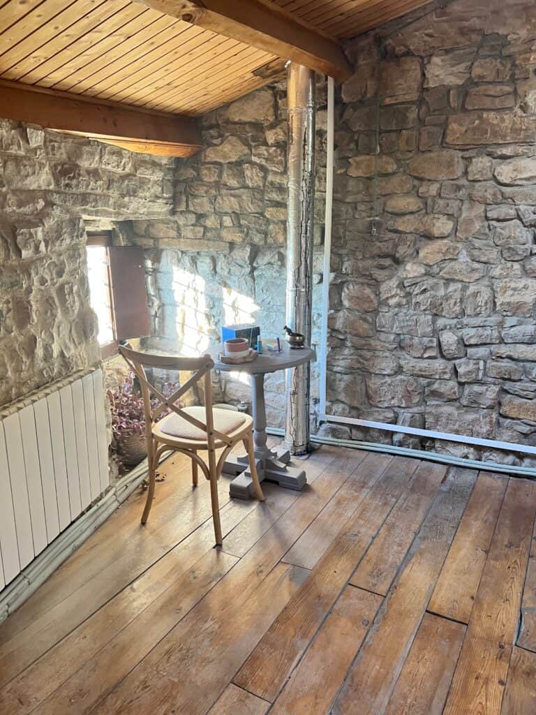 Cozy stone-walled workspace at Casa Pardal with a wooden chair, small round table, and warm morning light streaming through a rustic window.
